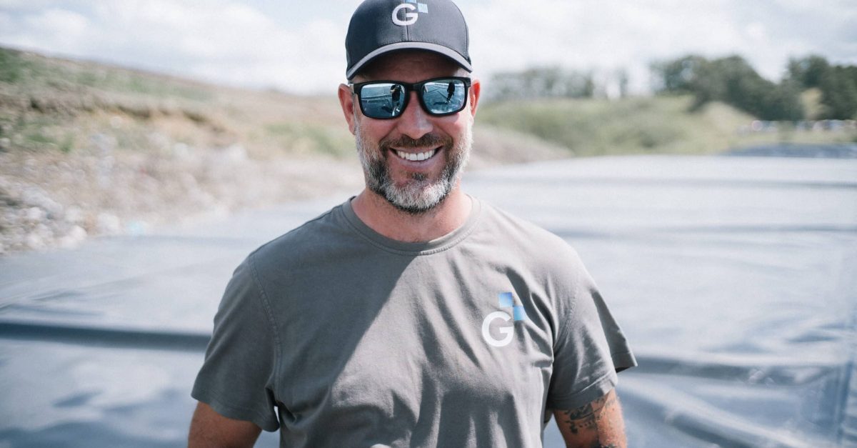 Portrait eines Mitarbeiters auf einer Deponie, er trägt eine Sonnenbrille und ein T-Shirt und eine Cap mit Logo.